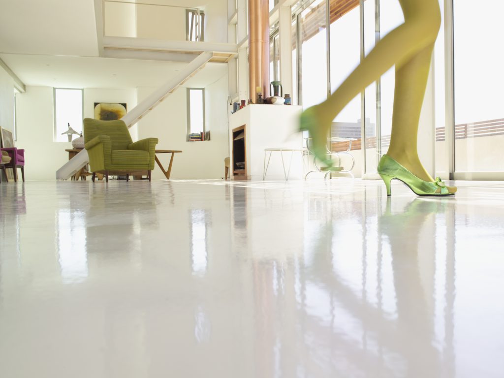 A woman is seen walking inside a modern, brightly lit building. The visible subject wears green heels and light yellow-green tights, showcasing the epoxy floor's durability in the Virginia summer. 

